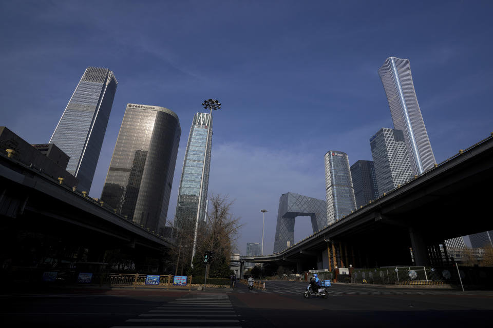 FILE - A food delivery worker rides through a quiet street against the backdrop of office buildings at the central business district in Beijing, Nov. 23, 2022. (AP Photo/Andy Wong, File)