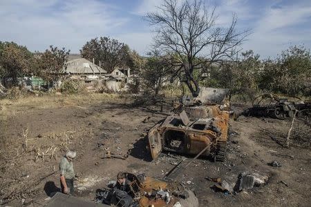 People stand near the burnt-out remains of Ukrainian armored vehicles in the village of Lutugine just outside Luhanks, eastern Ukraine, September 14, 2014. REUTERS/Marko Djurica