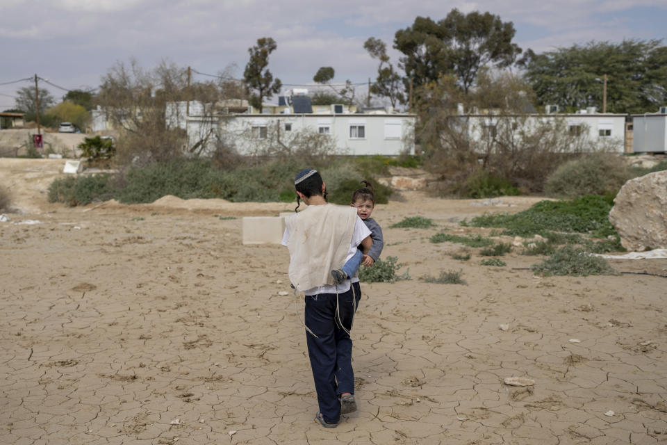 A settler youth carries his young brother at the West Bank Jewish outpost of Beit Hogla, Wednesday, Feb. 15, 2023. Israel's new ultranationalist government declared last week that it would legalize 10 unauthorized outposts in the occupied West Bank. The rare move intensified the country's defiance of international pressure and opened an aggressive new front of Israeli expansion into the West Bank, which Israel captured in the 1967 Mideast war. (AP Photo/Ohad Zwigenberg)