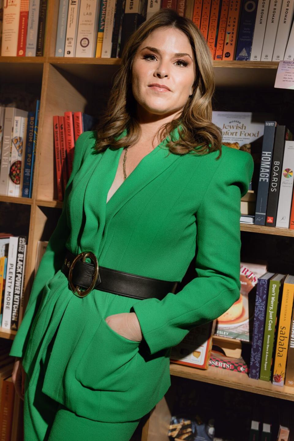 woman in a green business suit poses in front of a bookshelf