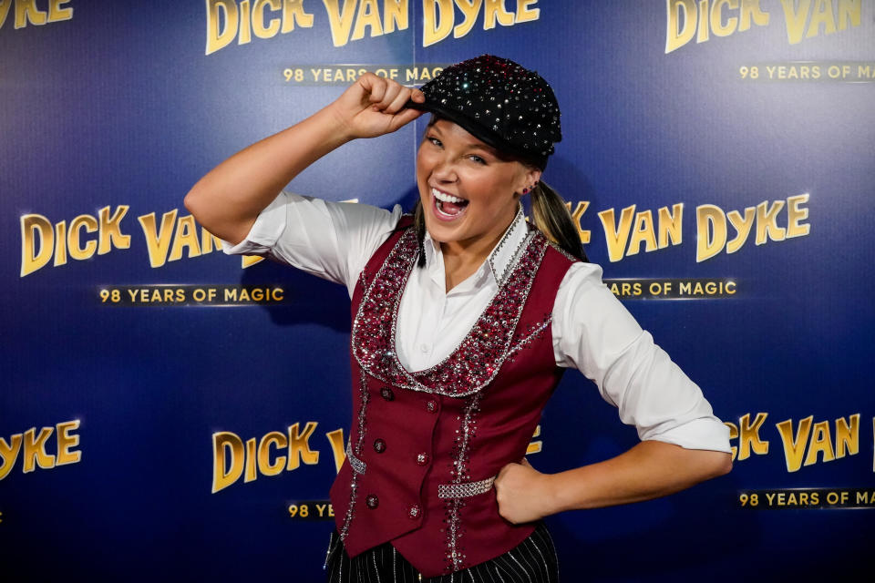 Person posing with a salute gesture at a Dick Van Dyke event, wearing a vest and embellished cap