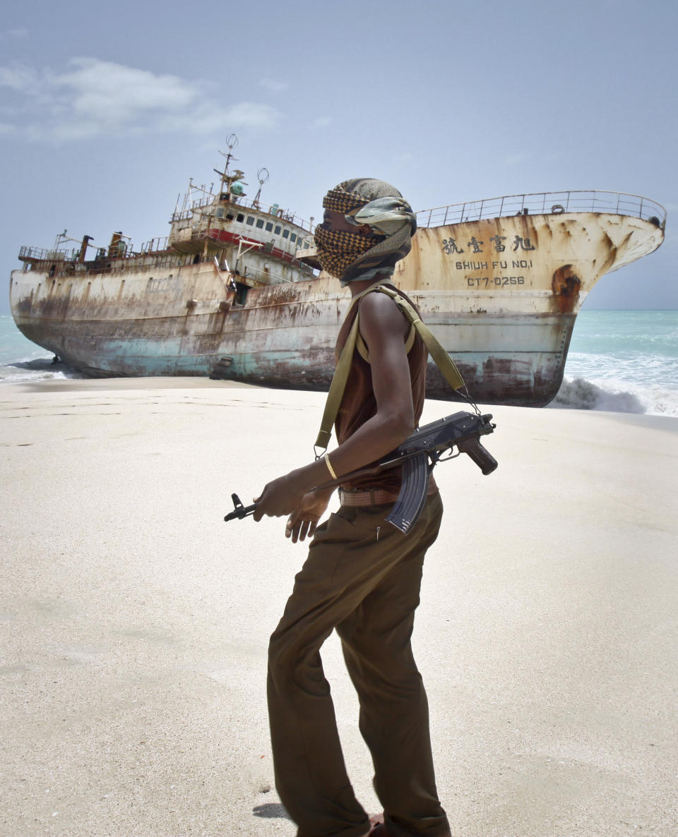 In this photo taken Sunday, Sept. 23, 2012, masked Somali pirate Abdi Ali walks past a Taiwanese fishing vessel that washed up on shore after the pirates were paid a ransom and released the crew, in the once-bustling pirate den of Hobyo, Somalia. The empty whisky bottles and overturned, sand-filled skiffs that litter this shoreline are signs that the heyday of Somali piracy may be over - most of the prostitutes are gone, the luxury cars repossessed, and pirates talk more about catching lobsters than seizing cargo ships. (AP Photo/Farah Abdi Warsameh)