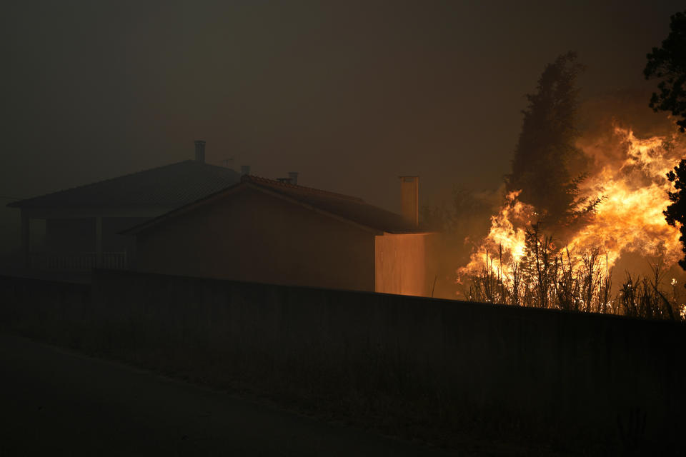 A forest fire reaches an empty house as smoke darkens the sky in the village of Bemposta, near Ansiao, central Portugal, Wednesday, July 13, 2022. Thousands of firefighters in Portugal continue to battle fires all over the country that forced the evacuation of dozens of people from their homes. (AP Photo/Armando Franca)