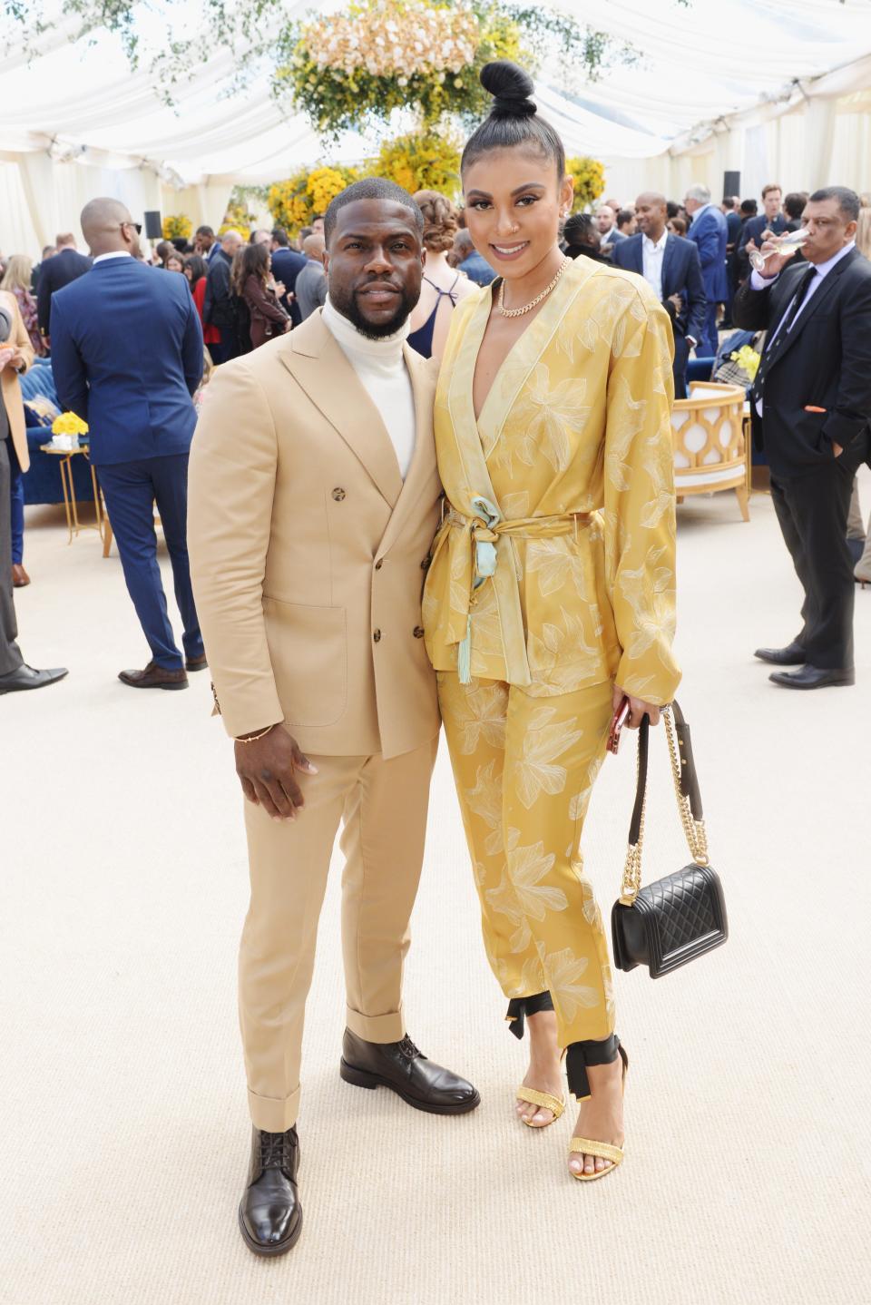 Eniko Parrish in a gold floral pant suit in heels standing taller than Kevin Heart in a coordinated yellow-cream suit and turtleneck.