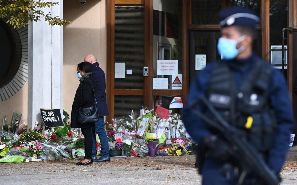 People look at flowers layed outside the Bois d'Aulne secondary school in homage to slain history teacher Samuel Paty - AFP