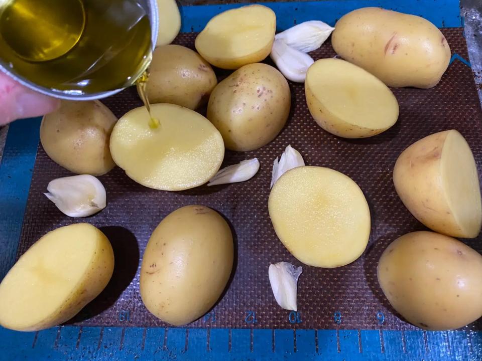 oil being poured over potatoes and garlic on a sheet pan