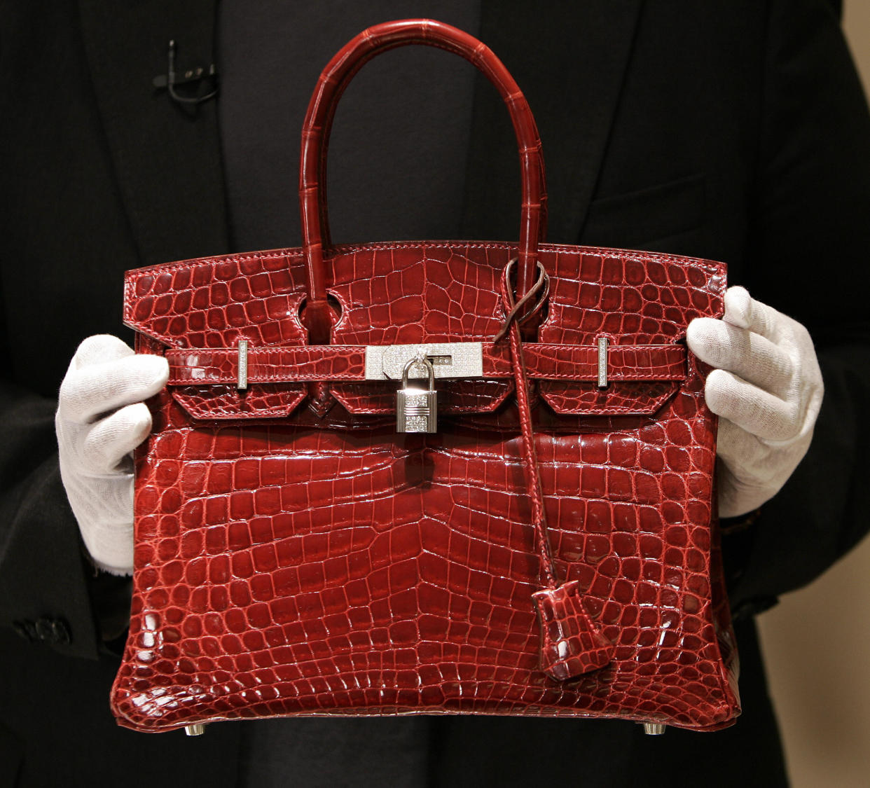 A person holding a red Hermes Birkin Bag made of crocodile leather.