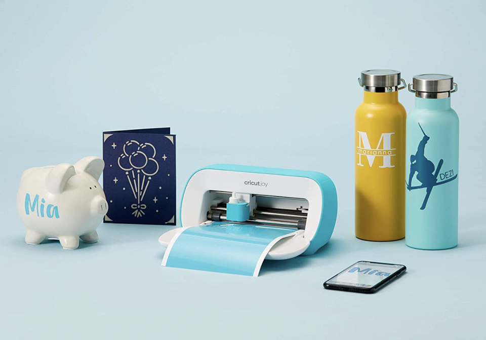 Cricut Joy machine with piggy bank, card and water bottles on blue background (photo via Amazon)