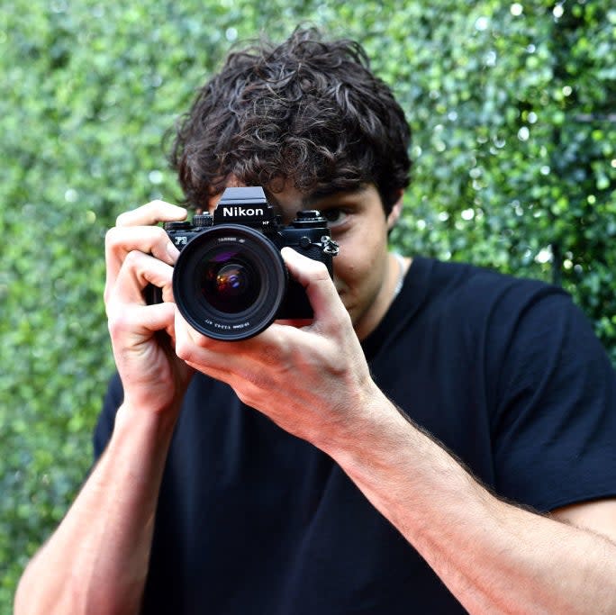Person holding a camera up to their face, taking a photo, with a green backdrop