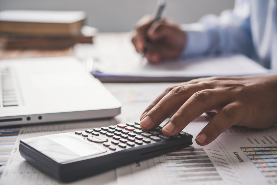 A man uses a calculator, laptop and pen at a desk.