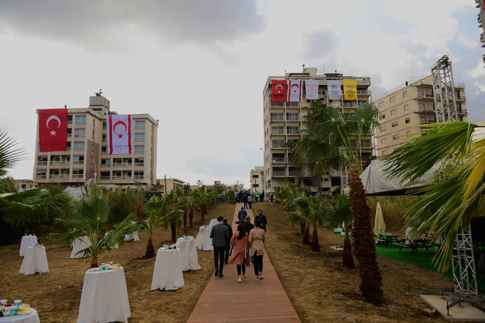 People walk at the decorates side in front of the abandoned buildings with a Turkish and Turkish Cypriots breakaway flags, before Turkish President Recep Tayyip Erdogan inspects the newly opened beachfront of Varosha in war-divided Cyprus' in the Turkish occupied area in the breakaway Turkish Cypriot north on Sunday, Nov. 15, 2020. Erdogan appeared to throw a fresh bid to restart dormant Cyprus reunification talks into doubt, saying that a two-state deal rather than the long-established federal formula is the way forward. (AP Photo/Nedim Enginsoy)