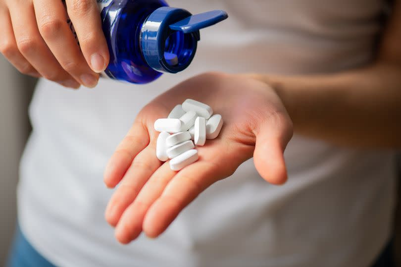 Close-up Females palm hand holding White Pills Calcium Capsule in hand and medicines in bottle standing by at home