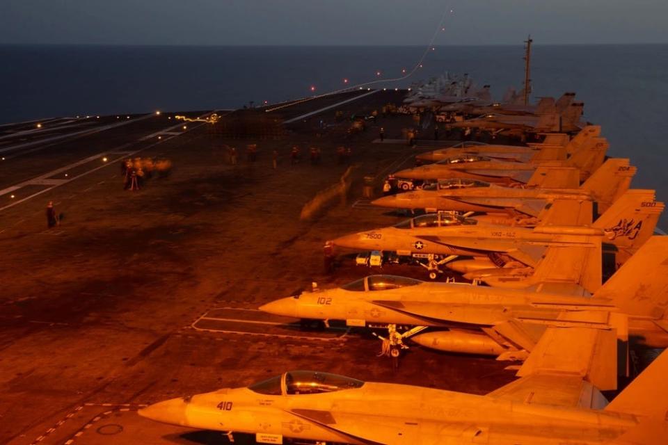 military aircraft board an aircraft carrier are illuminated in red-tinted light