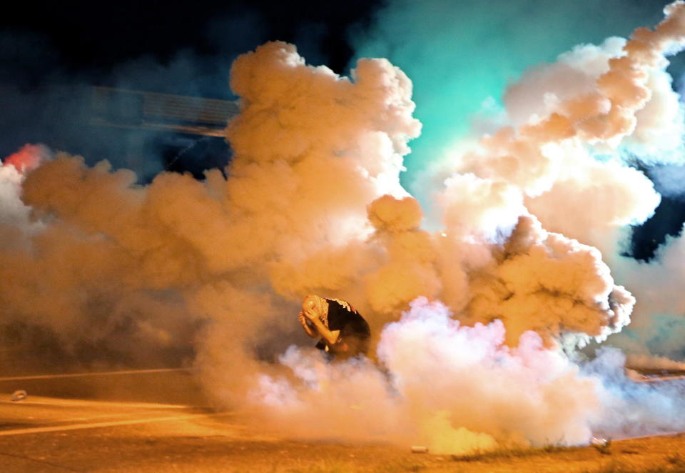 <p>Aug 13, 2014 – Ferguson, Missouri, U.S. – A protester takes shelter from tear gas canisters exploding around him on West Florissant Ave. On this night protesters attempted to throw Molotov cocktails, rocks and bottles at police. This was the four straight night police used tear gas to disperse crowds protesting the death of Michael Brown. (David Carson/St Louis Post-Dispatch/ZUMAPRESS.com) </p>