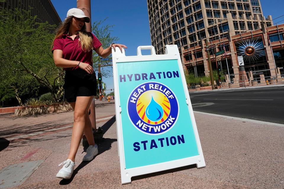 Julia Marturano, of the City of Phoenix Heat Response Program, places a sign out on a sidewalk in July 2023 directing those who needed water and other items to a hydration station as temperatures reached 119-degrees.