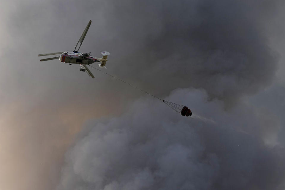 A helicopter works to extinguish fire at burning warehouse of the online retailer Ozon in Istra Municipal District, northwest Moscow Region, Russia, Wednesday, Aug. 3, 2022. The fire, which erupted at the warehouse belonging to Russia's leading online retailer Ozon, has covered the area of 50,000 square meters and injured 11 people, two of whom were hospitalized. (AP Photo/Alexander Zemlianichenko)