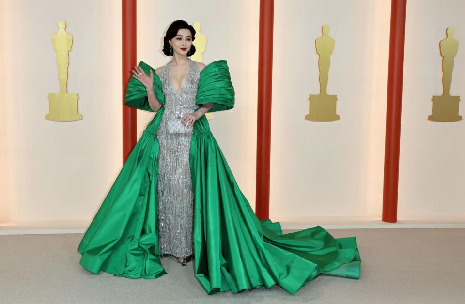 Fan Bingbing in a shimmering silver gown with green, cape-like sleeves and wrap-around, trailing green skirt.