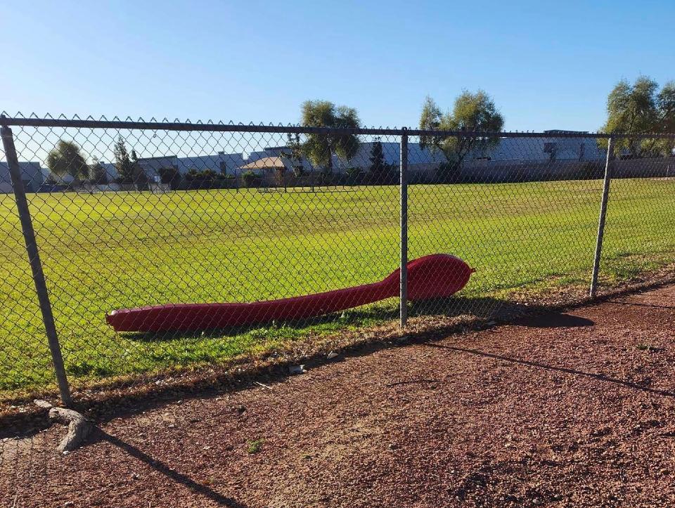 This photo provided by Michael Foster shows a 15-foot red spoon lying behind a fence in Phoenix on Monday, April 3, 2023. Foster found the giant red spoon while playing Pokemon GO. It was stolen from an Arizona Dairy Queen on March 25 and sparked a mystery on social media.