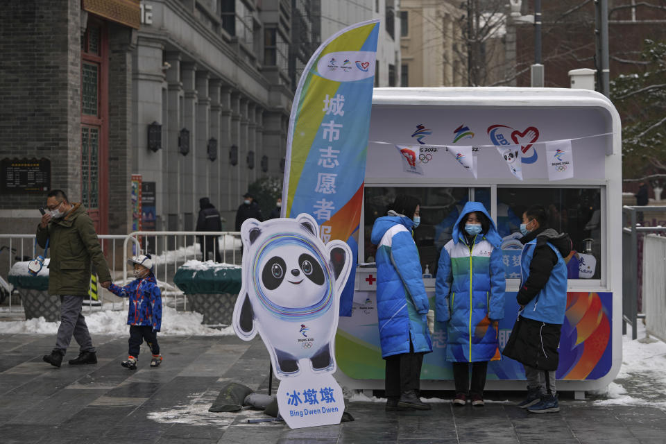 Volunteers wearing face masks to help protect from the coronavirus chat each others at an information booth for Beijing Winter Olympics Games at Qianmen Street, a popular tourist spot in Beijing, Sunday, Jan. 23, 2022. Chinese authorities have called on the public to stay where they are during the Lunar New Year instead of traveling to their hometowns for the year's most important family holiday. (AP Photo/Andy Wong)