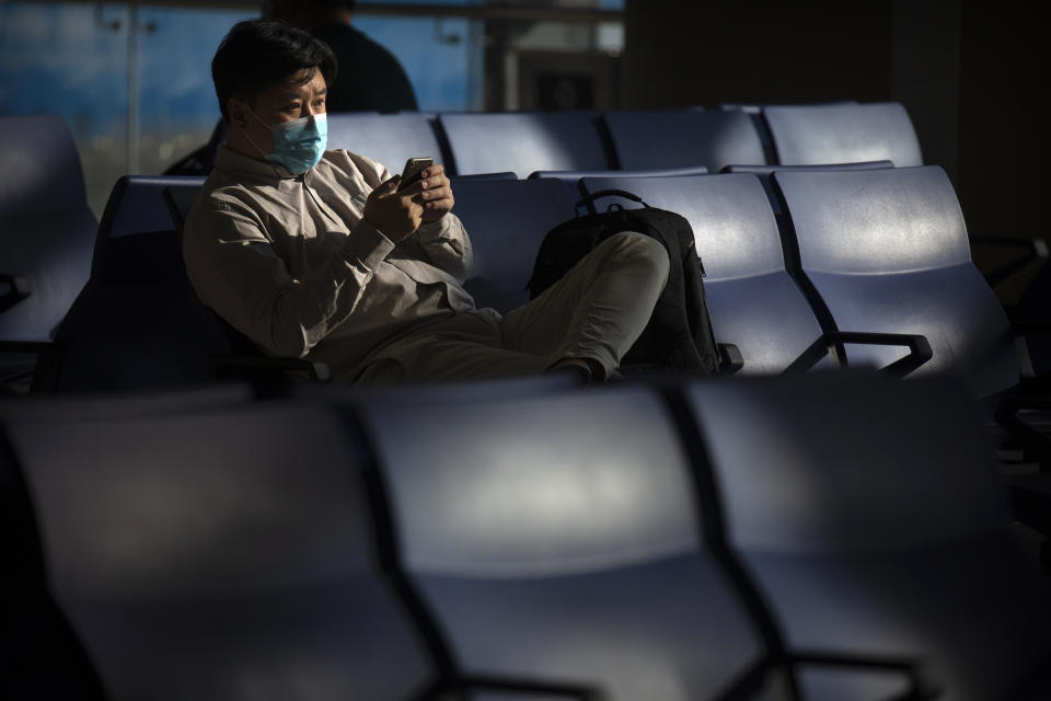 A traveler wearing a face mask to protect against the coronavirus sits at a boarding gate at the Shanghai Hongqiao International Airport in Shanghai, Friday, Nov. 6, 2020. With the COVID-19 outbreak largely under control within its borders, air travel in China has mostly returned to pre-pandemic levels. (AP Photo/Mark Schiefelbein)