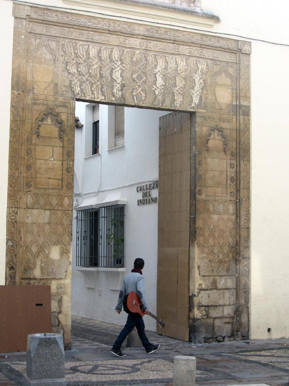 This Jan. 12, 2013 show a man carrying a guitar walking past a Moorish gate in the historic downtown of Cordoba, in Andalusia, Spain. Andalusia offers a fusion of Christian and Islamic cultures, found in architectural masterpieces and in everyday life. (AP Photo/Giovanna Dell’Orto)