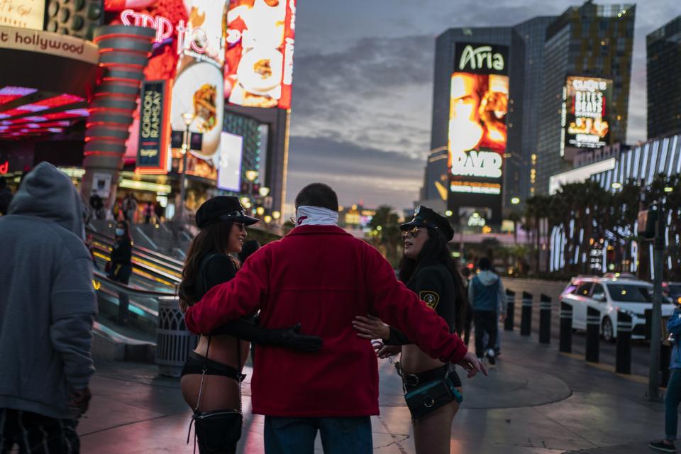 Women dressed as scantily-clad police officers pose for photos with a man on the Las Vegas Strip, Wednesday, Nov. 11, 2020. Las Vegas sells itself on fantasies of wealth, luxury, and sex, and even the most cynical first-time visitor can come here expecting at least a hint of James Bond playing baccarat in Monte Carlo. That would be a mistake. Vegas feels more like a mixture of the endless mall and Disney-ish resort set to the music of amplified slot machines. Gamblers wear jeans and shorts, not tuxedoes. (AP Photo/Wong Maye-E)