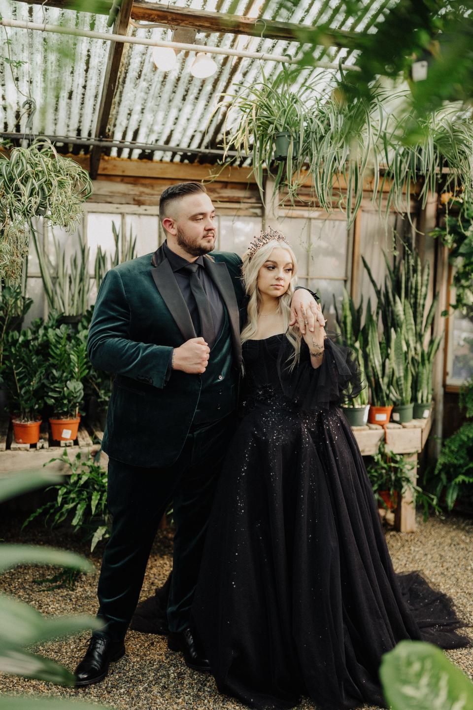 A bride and groom pose in a greenhouse in their wedding attire.