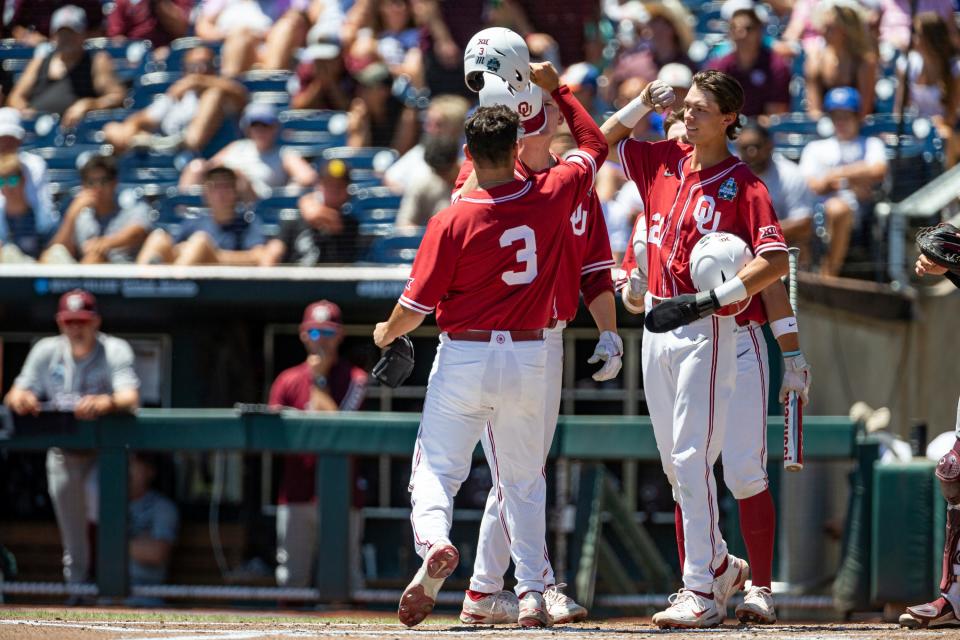 Oklahoma's Jimmy Crooks (3) bumps helmets with Peyton Graham (20) and Blake Robertson (26) celebrating his three run homer in the first inning against Texas A&M during an NCAA College World Series baseball game Wednesday, June 22, 2022, in Omaha, Neb. (AP Photo/John Peterson)