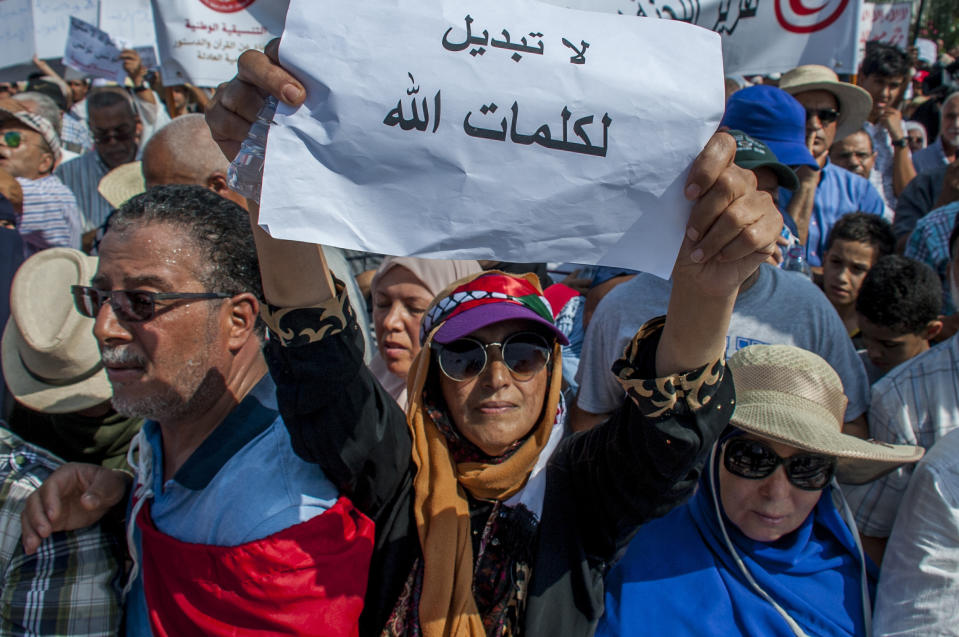 People demonstrate, one with a poster reading "No to change God's speech" during a demonstration in Tunis, Saturday Aug 11, 2018. Thousands of Muslim fundamentalists have held an hours-long protest in front of the nation's parliament to decry proposals in a government report on gender equality. (AP Photo/Hassene Dridi)