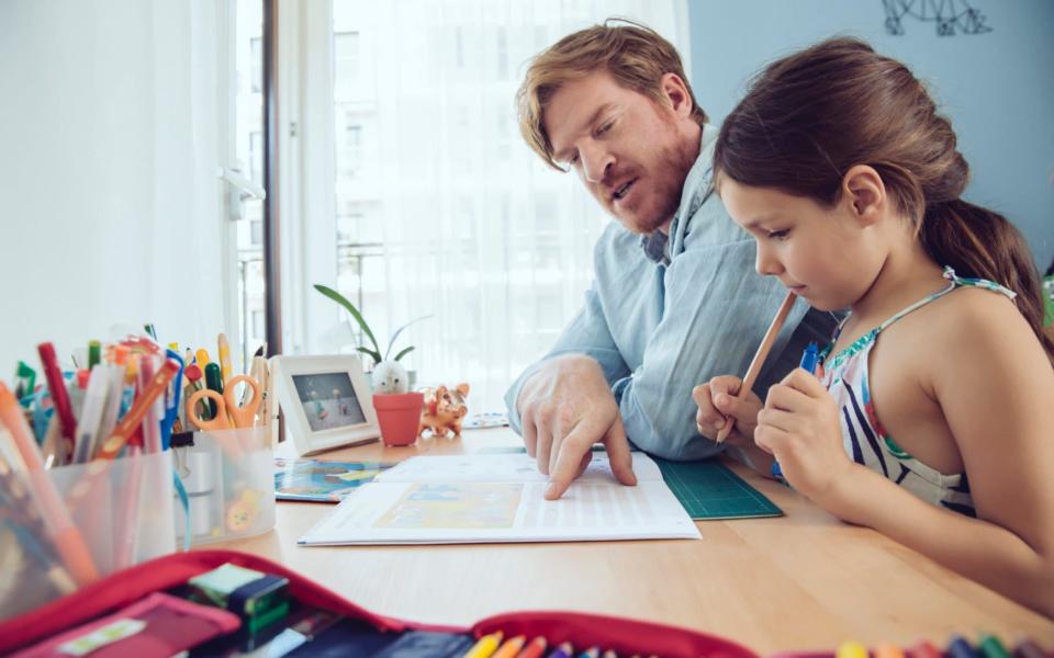 Father helping girl doing her schoolwork at home - Getty Images Contributor