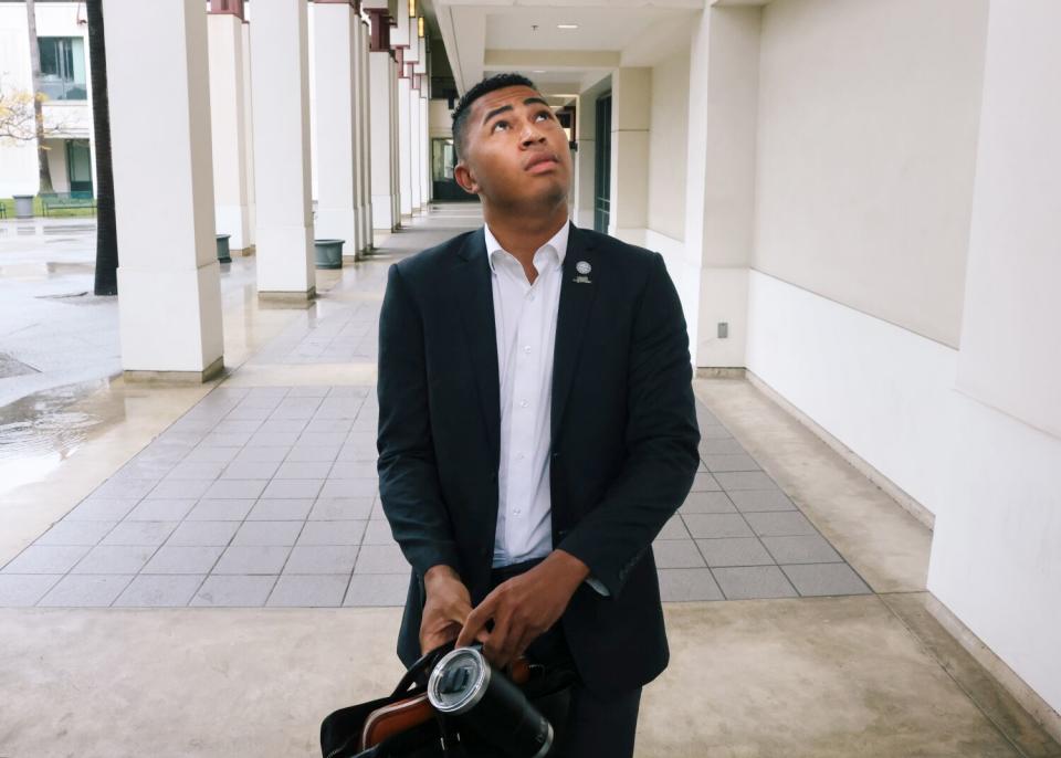 Dressed in a suit, Triston Ezidore walks down a columnway, looking up.