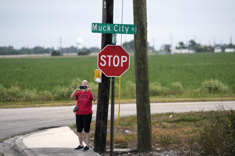 A woman films with her phone at the corner of Muck City Road, as farmworkers and allies set off on a five-day trek aimed at highlighting the Fair Food Program, which has enlisted food retailers to use their clout with growers to ensure better working conditions and wages for farmworkers, Tuesday, March 14, 2023, in Pahokee, Fla. (AP Photo/Rebecca Blackwell)