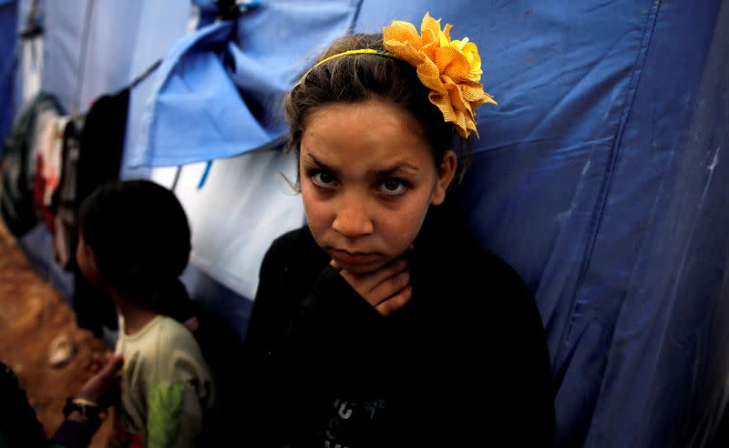An internally displaced Syrian girl stands next to a tent in an IDP camp located near Idlib