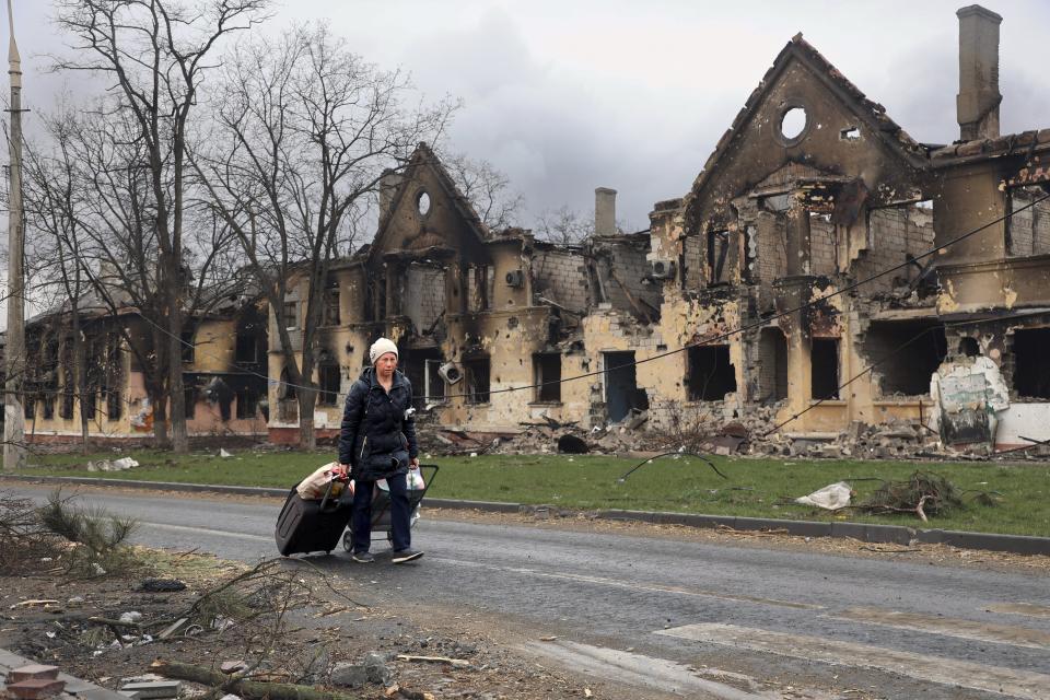 A woman pulls her bags past houses damaged during fighting in eastern Mariupol, Ukraine, Friday, April 8. Ukraine says it is investigating a claim that a poisonous substance was dropped on the besieged city of Mariupol.