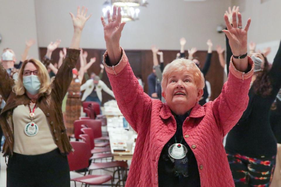 A woman standing and holding her hands up high amidst other people, doing the same.