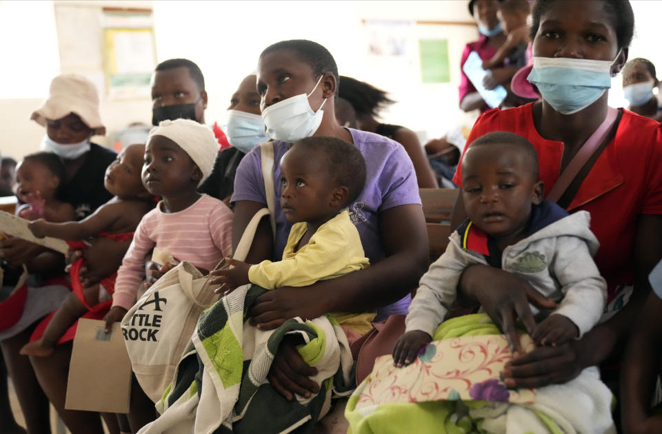 Women holding babies take their places on wooden benches at a clinic in Harare, Zimbabwe, Thursday, Sept. 15, 2022. Church members in Zimbabwe are getting their children vaccinated against measles in secret amid a deadly outbreak. It's to avoid being shunned by religious leaders who are opposed to modern medicine. (AP Photo/Tsvangirayi Mukwazhi)