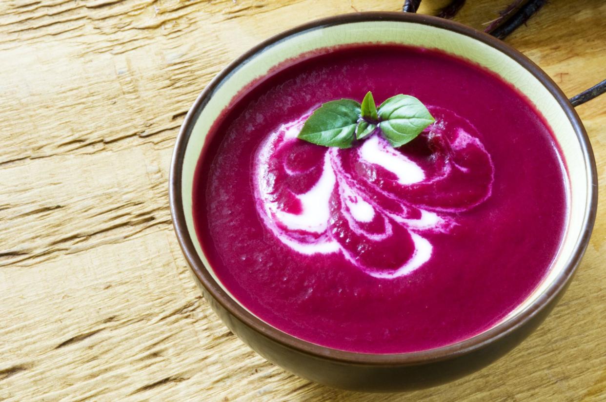 A bowl of beet soup with a swirl of yogurt, basil and black pepper.