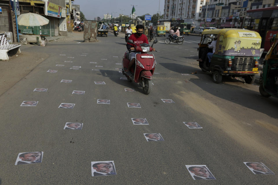 Indian commuters move on defaced images of French President Emmanuel Macron pasted by protestors on a road in Ahmedabad, India, Sunday, Nov. 1, 2020. Muslims have been calling for both protests and a boycott of French goods in response to France's stance on caricatures of Islam's most revered prophet. (AP Photo/Ajit Solanki)