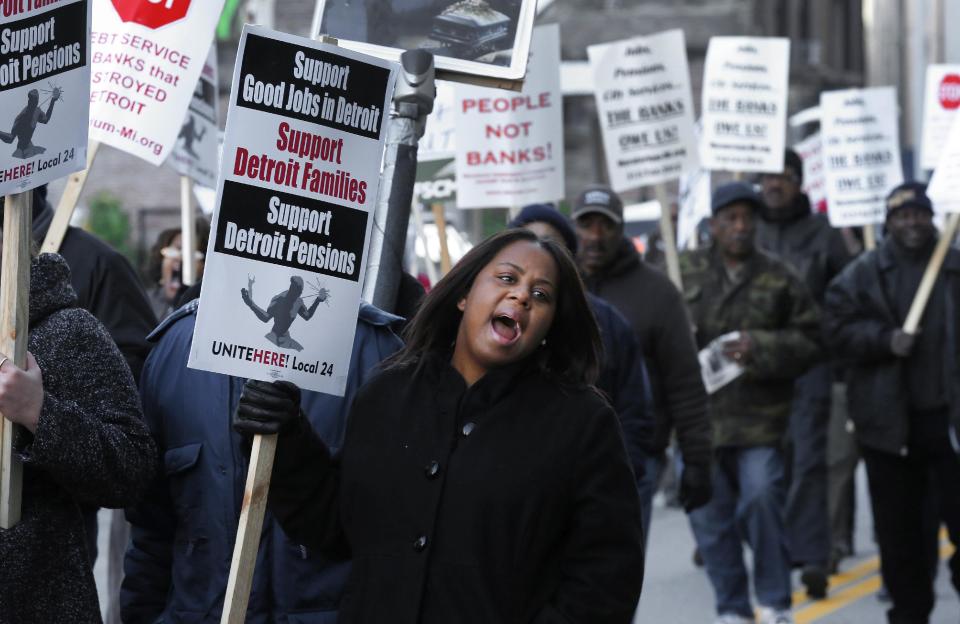 FILE- In this Oct. 23, 2013 file photo, Jalita Shabazz joins protesters during a rally outside The Theodore Levin United States Courthouse in Detroit. The city of Detroit reached tentative agreements to preserve pensions for retired police office and firefighters but cut monthly payments for other former employees, officials said Tuesday, April 15, 2014. (AP Photo/Paul Sancya, File)