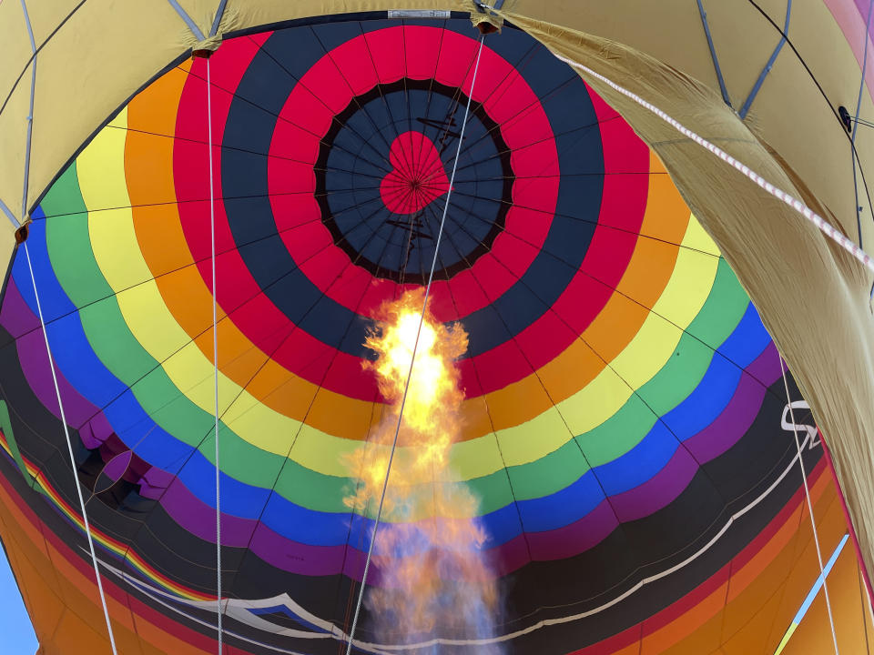 The flame of a gas burner helps inflate a hot air balloon as part of a re-enactment of the first Albuquerque International Balloon Fiesta in 1972 during a special event at Coronado Center in Albuquerque, New Mexico, on Friday, Sept. 30, 2022. Hundreds of hot air balloons will be lifting off over the nine-day annual fiesta that has drawn pilots and spectators from across the globe for 50 years. (AP Photo/Susan Montoya Bryan)