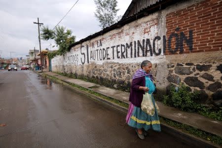 An elderly woman walks past a graffiti reading "No political parties, Yes to self-determination" in the indigenous Purepecha town of Arantepacua, in Michoacan state, Mexico June 28, 2018. Picture taken June 28, 2018. REUTERS/Alan Ortega