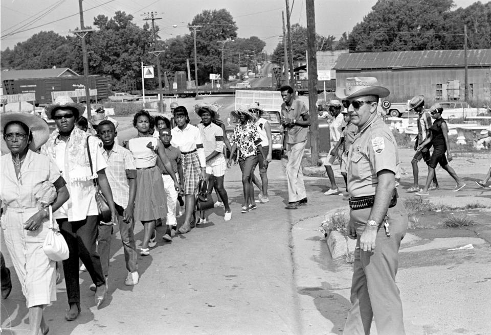 <p>Neshoba County Deputy Sheriff Cecil Price watches marchers as they pass through Philadelphia, Miss., during a memorial for three slain civil rights workers, June 21, 1965. Price is charged with conspiracy to violate the civil rights of the three Freedom Summer activists slain by Klansmen in 1964. Seven Ku Klux Klansmen were convicted of federal civil rights violations in the deaths and sentenced to prison terms ranging from three to ten years; none served more than six years. (Photo: Jack Thornell/AP) </p>