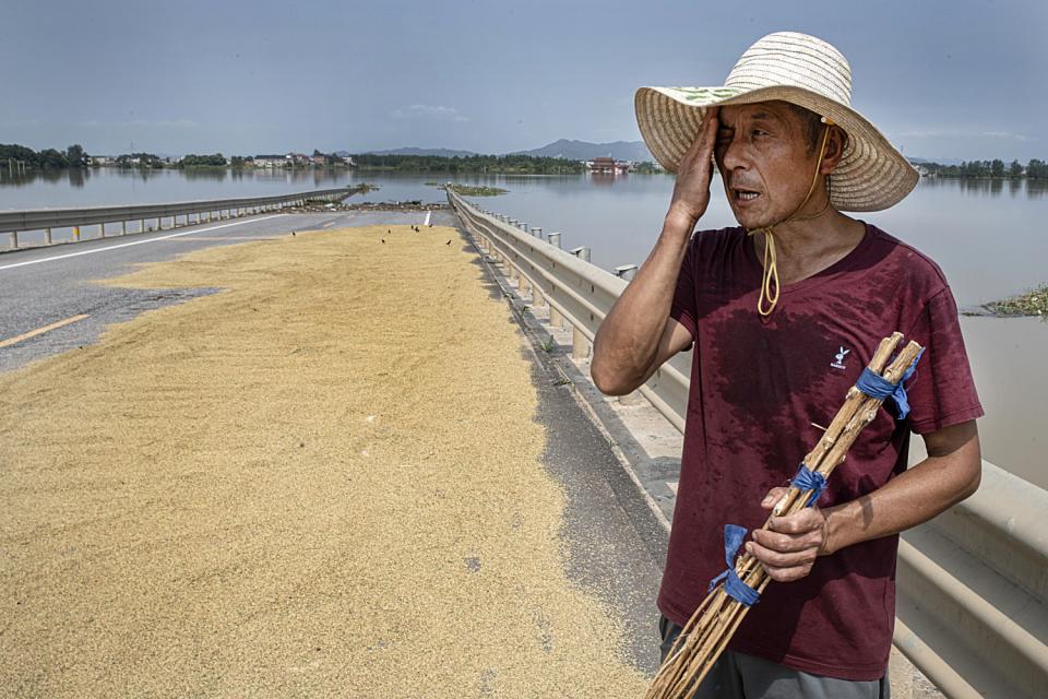 Sheng, a local farmer, lays out rice seeds to dry on a flooded road, surrounded by his flooded farms.