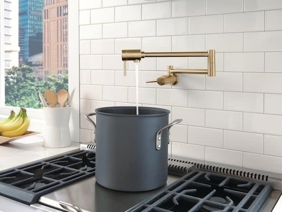 gold-tone pot filler faucet above black stove