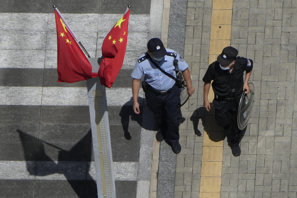 A policeman, right, and security guard walk past Chinese flags outside the Evergrande headquarters in Shenzhen, China, Friday, Sept. 24, 2021. Things appeared quiet at the headquarters of the heavily indebted Chinese real estate developer Evergrande, one day after the day it had promised to pay interest due to bondholders in China. (AP Photo/Ng Han Guan)