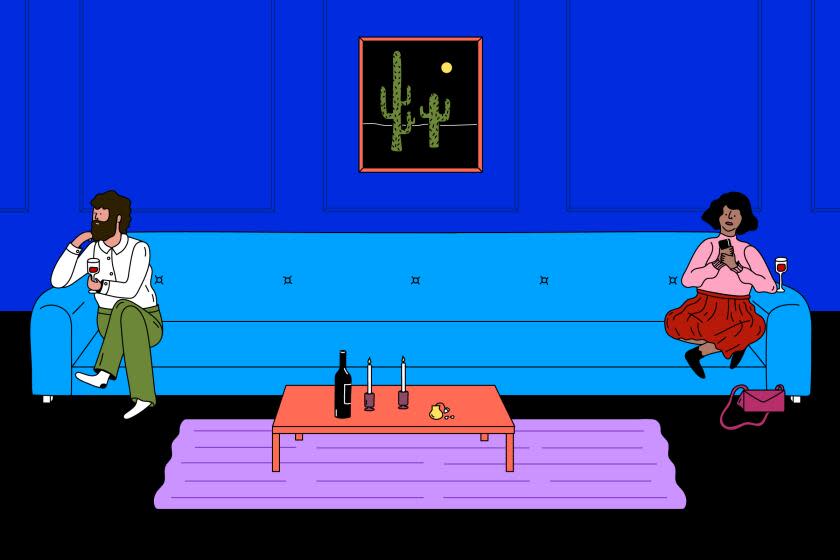 man & woman on a date sit awkwardly on different ends of a very long blue couch with a dark blue wall with a cactus painting