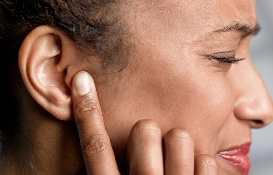a woman making a pained face touching her ear