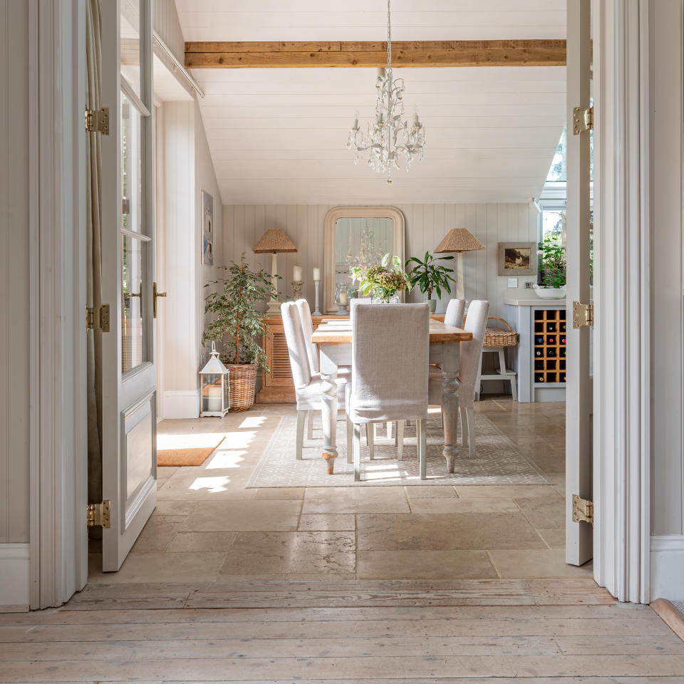 View from the hallway with wooden floor to the dining room with stone floor and neutral furniture