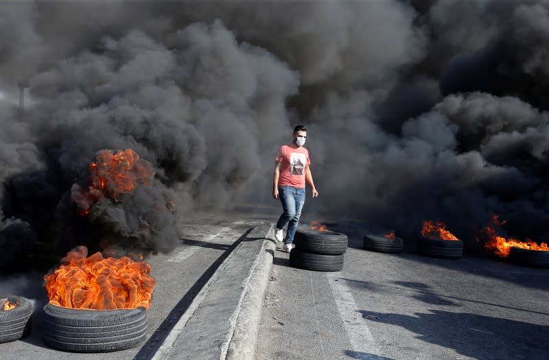 A demonstrator walks near burning tires barricading a road during ongoing anti-government protests in Khaldeh