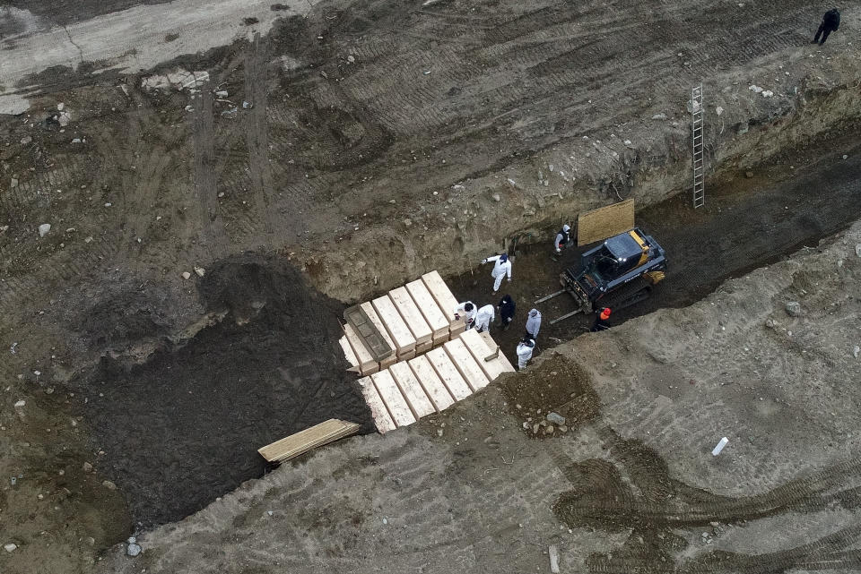 Workers wearing personal protective equipment bury bodies in a trench on Hart Island, Thursday, April 9, 2020, in the Bronx borough of New York. On Thursday, New York City’s medical examiner confirmed that the city has shortened the amount of time it will hold on to remains to 14 days from 30 days before they will be transferred for temporary internment at a City Cemetery. Earlier in the week, Mayor Bill DeBlasio said that officials have explored the possibility of temporary burials on Hart Island, a strip of land in Long Island Sound that has long served as the city’s potter’s field. (AP Photo/John Minchillo)